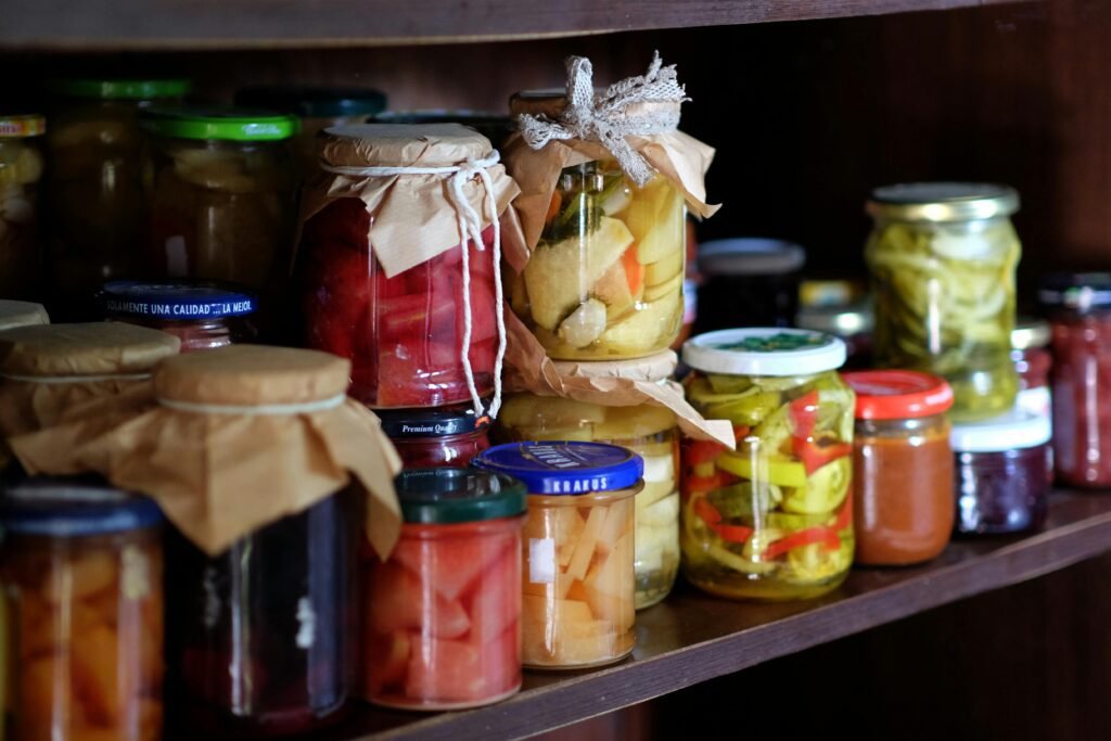 A variety of homemade preserves and pickles stored on a rustic wooden pantry shelf.