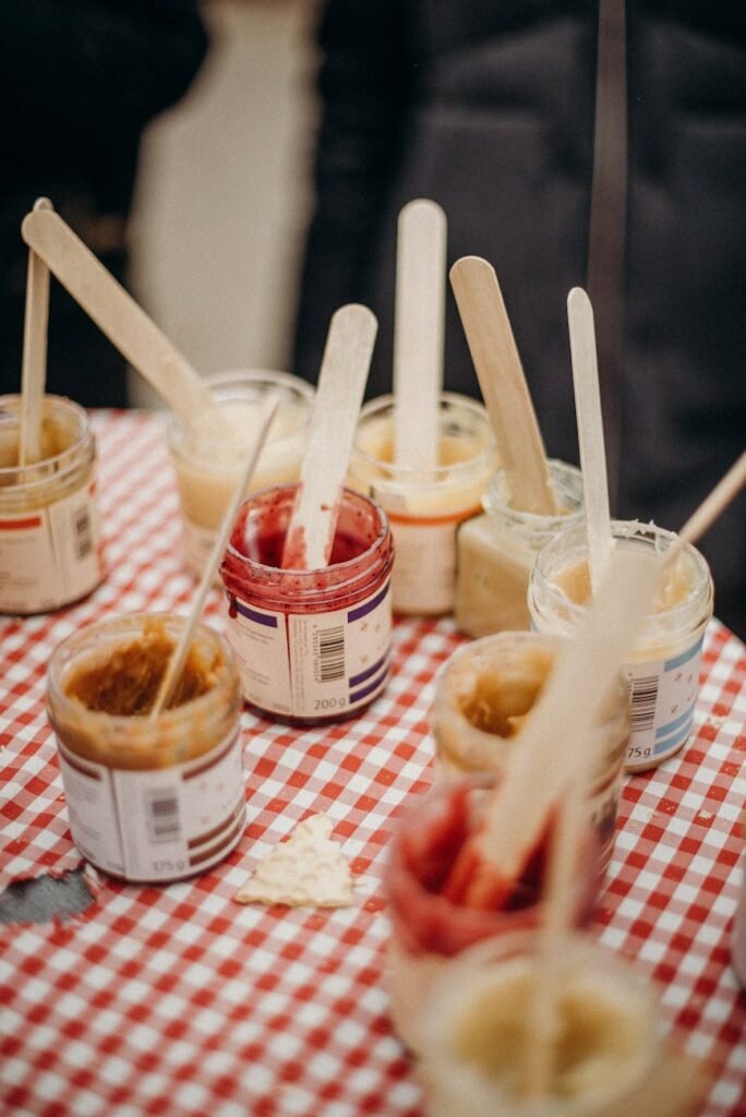 Close-up of various jam jars on a red checked tablecloth with wooden spoons, ideal for food market scenes.
